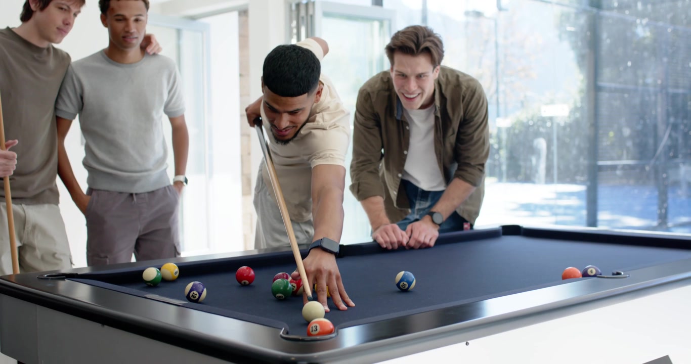 Diverse male pals playing pool African American man lining, striking cue ball breaking rack at home