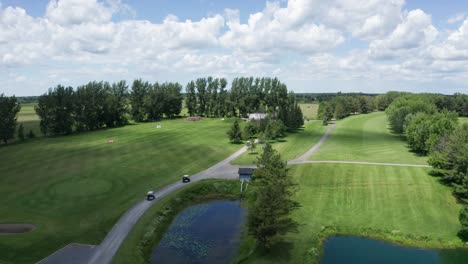 Drone-follows-golf-carts-on-path-beside-long-straight-fairway-of-golf-course-as-tournament-begins