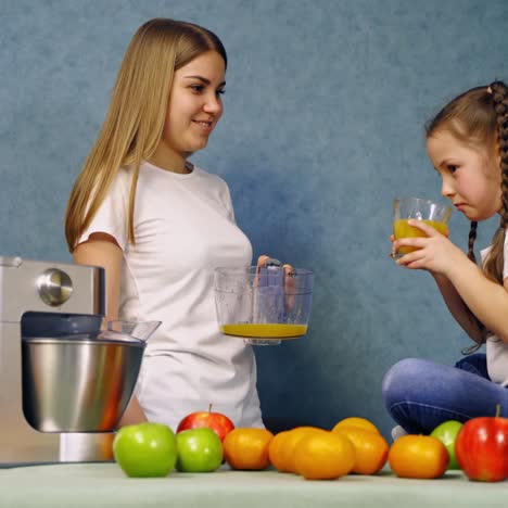 mother and daughter in the kitchen. little girl drinks freshly squeezed juice. healthy drink. organic fruit and a modern squeezer on the table.