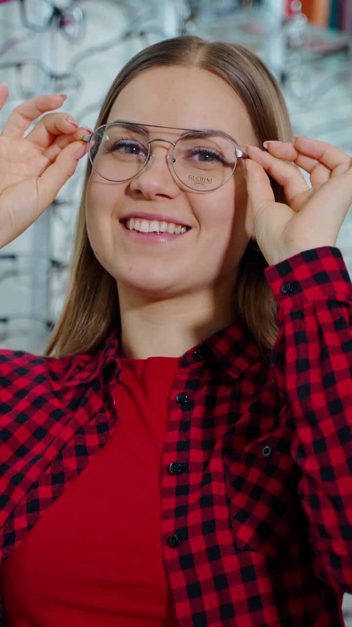 Portrait of a happy woman trying on trendy eyeglasses. Smiling female buyer choosing new glasses and posing on camera in optic store. Vertical video