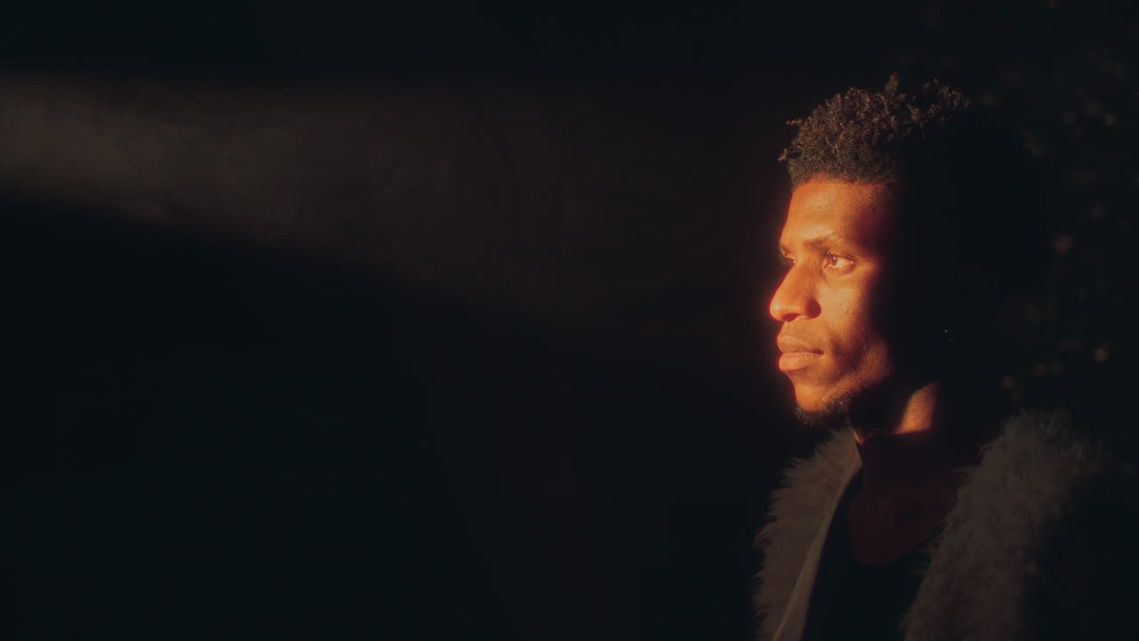 African American Man Standing in Beam of Golden Light against Dark Background