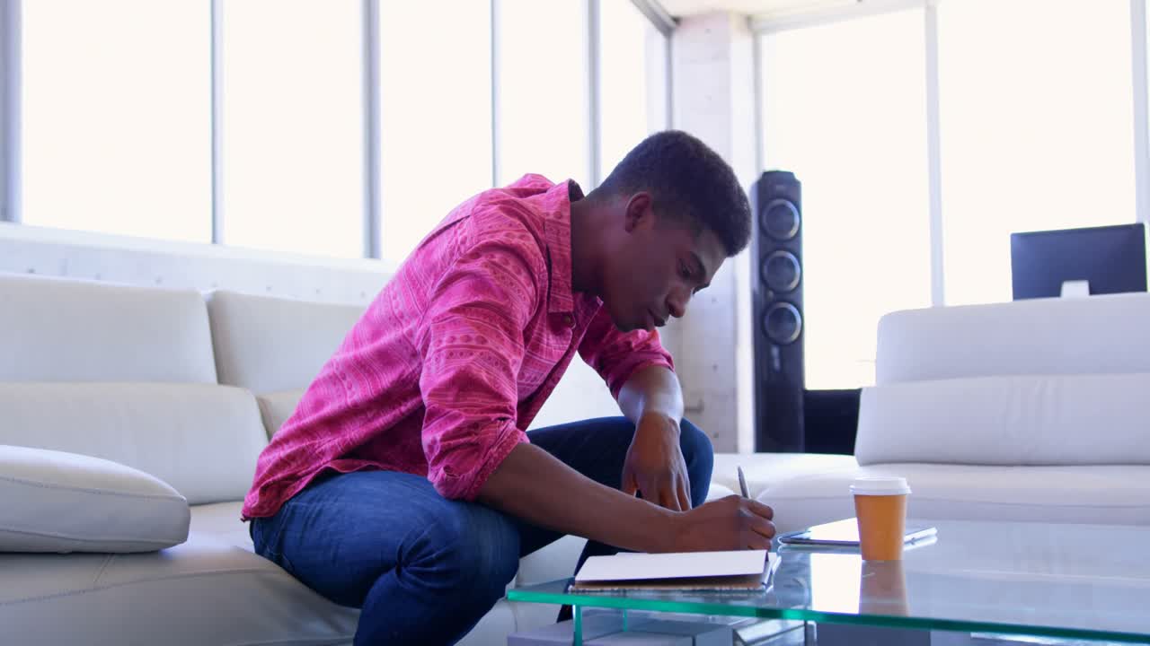 Handsome African american male executive writing on a diary in modern office 4k