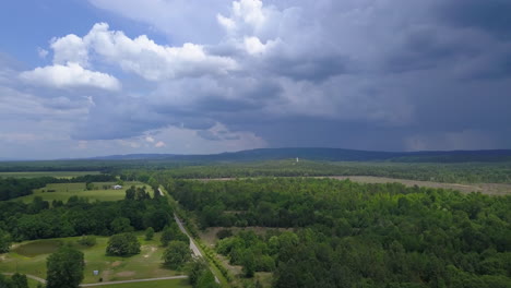 Panorámica-Lenta-De-Izquierda-A-Derecha-Toma-Aérea-De-Un-Paisaje-Rural-De-Verano-Y-Tierras-De-Cultivo-Con-Nubes-De-Tormenta-En-La-Distancia