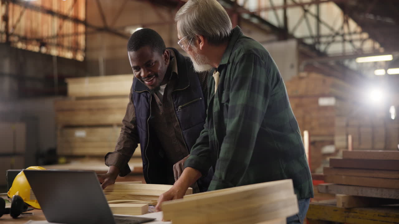 Two men working with wood and a laptop in a workshop