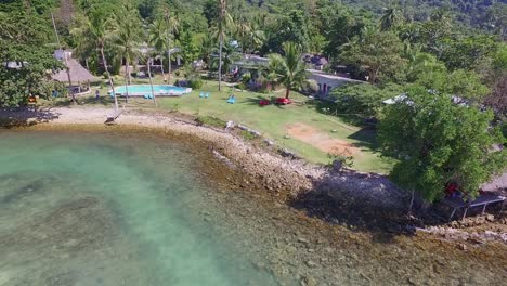 panning out drone shot of small bungalow resort in thailand with swimming pool and surrounding ocean and coral reef