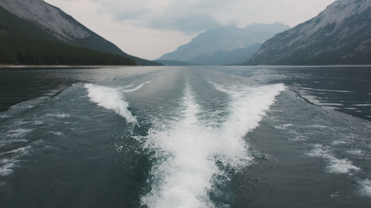 Boat's wake ripples across the pristine waters of Lake Minnewanka in Banff, surrounded mountains