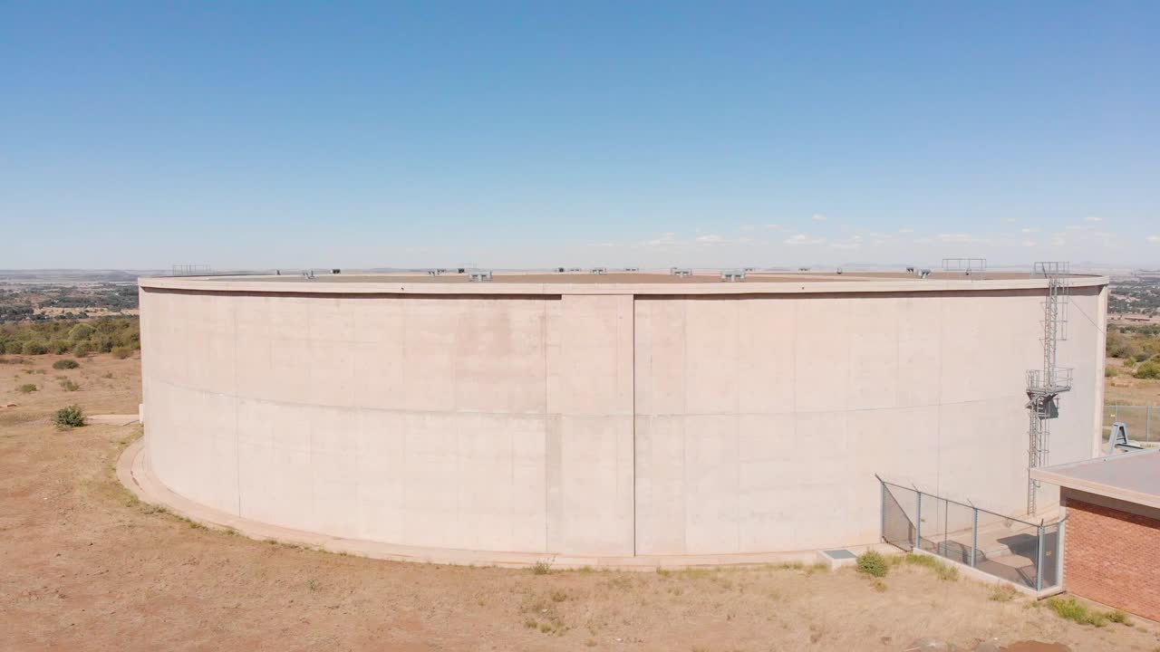 Ripresa rivelatrice da drone di un serbatoio d'acqua che fornisce acqua a una città sullo sfondo in una giornata di sole.