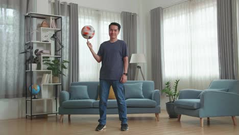 asian man spin soccer ball on finger in living room