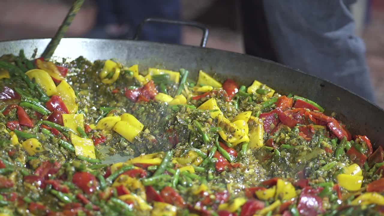 Primo piano della preparazione di un risotto di verdure con molti ingredienti in una grande padella aperta