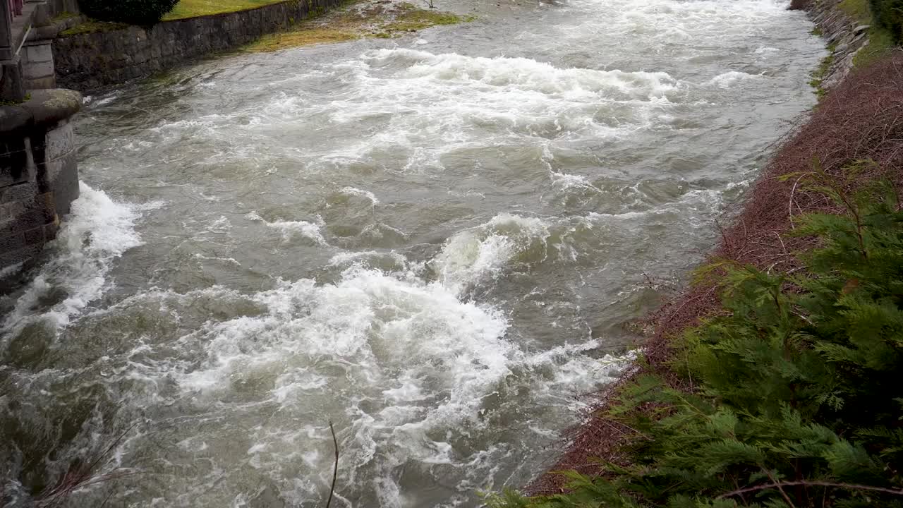 Vista da drone di acqua torbida che scorre velocemente rilasciata da una diga idroelettrica, circondata dalla vegetazione e che mostra l'infrastruttura di generazione di energia in Cornovaglia, Inghilterra
