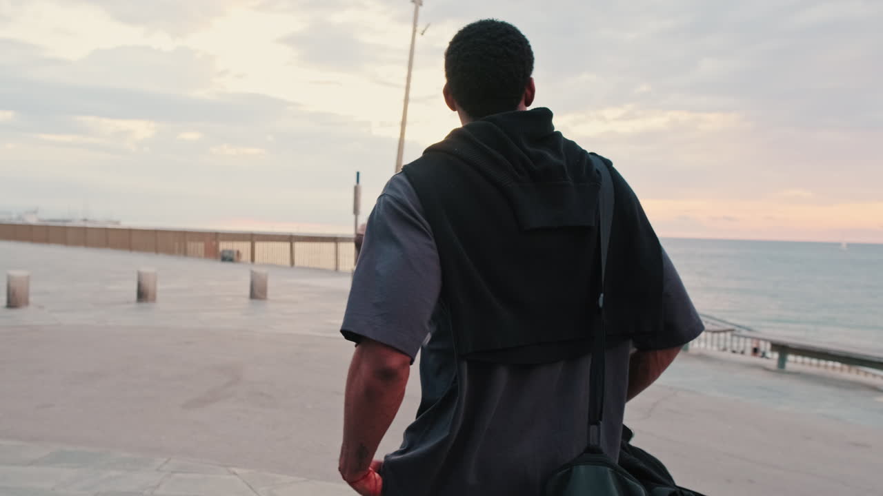 Young Man Walking Along Seaside Promenade at Sunset