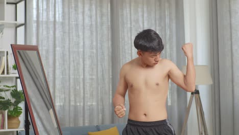 아시아 십대 소년 이 집 에서 셔츠 를 벗고 운동 을 한 후, 팔꿈치 를 구부리고 거울 을 바라보고 있다