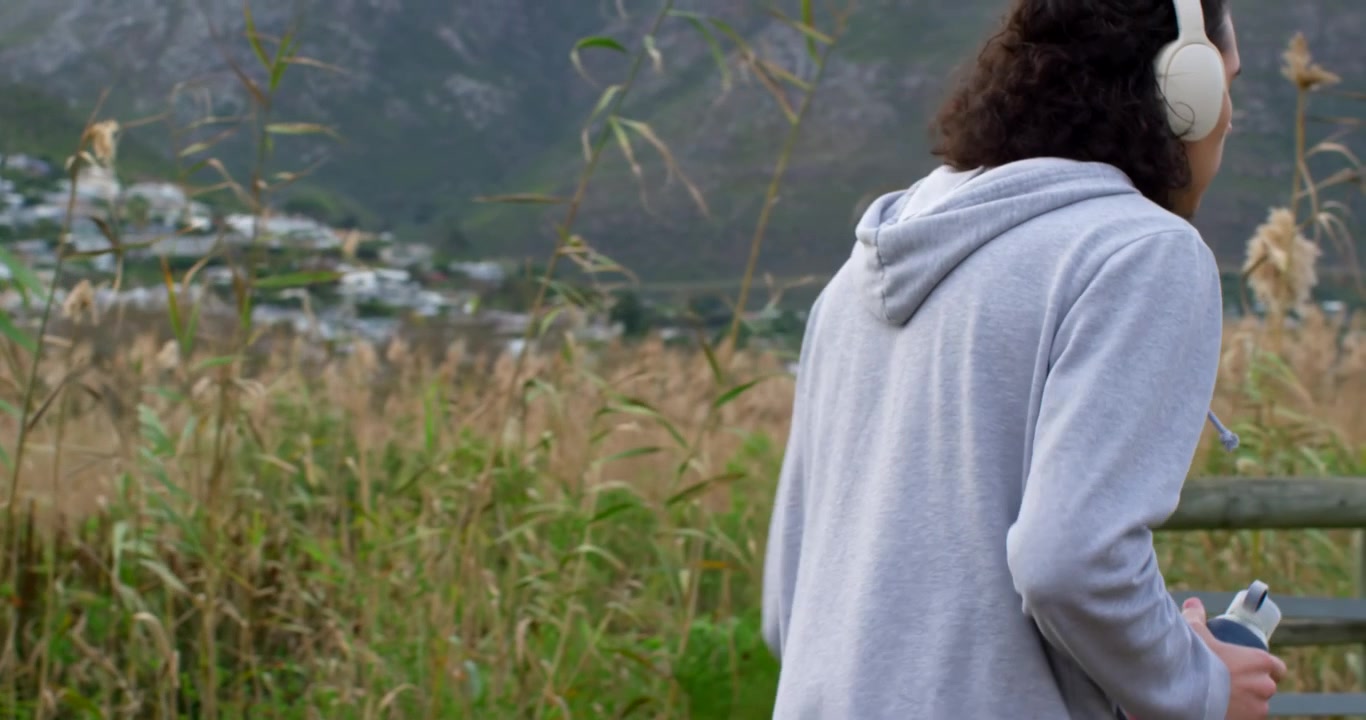 African American man shifting, walking then jogging along marsh with headphones, bottle for fitness