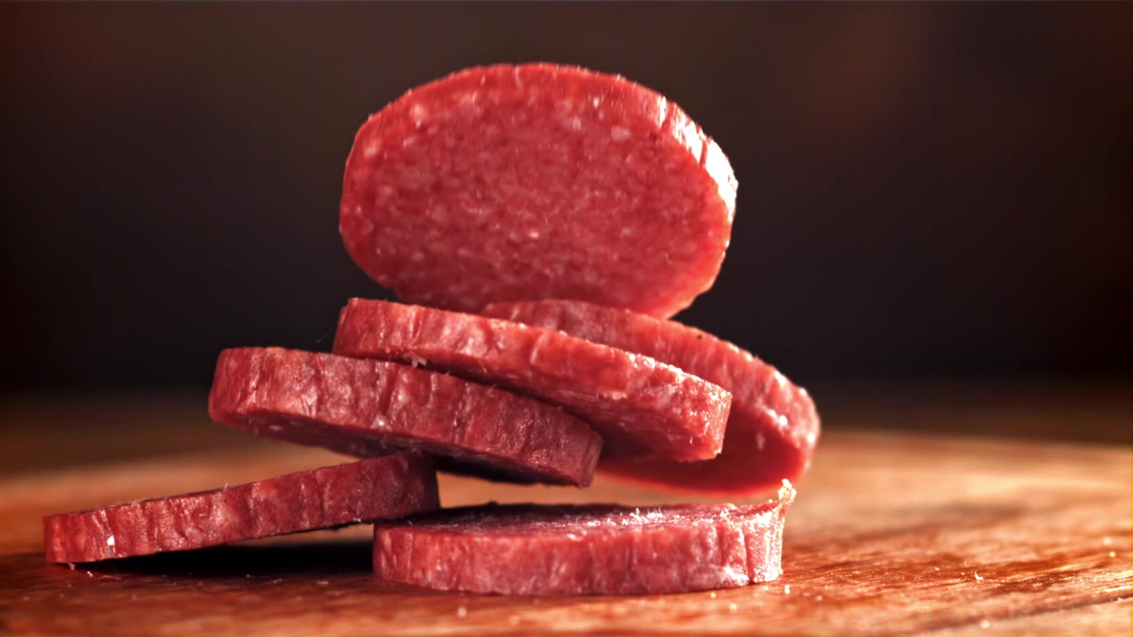 Spadające i układające się w stos plasterki salami na drewnianej powierzchni