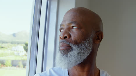 side view of mature black man looking through window in a comfortable home 4k