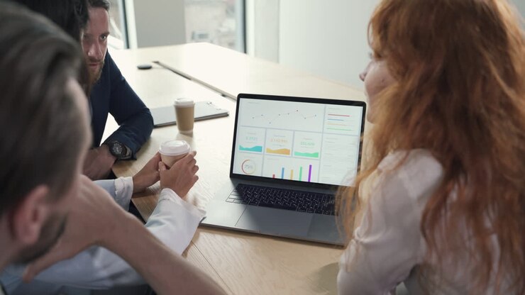 A young working team composed of two women and two men consulting financial results at the laptop in a work meeting