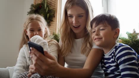 Mamá-Y-Niños-Usando-Un-Teléfono-Inteligente-En-La-Mañana-De-Navidad