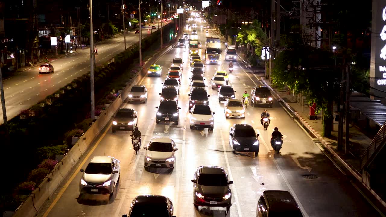 Busy Sathorn Road with cars and motorcycles under bright streetlights, overhead static camera, nighttime