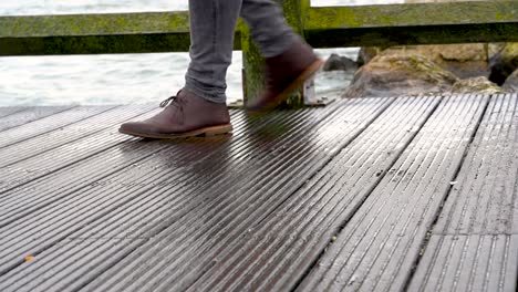 close-up view of man's legs in jeans and brown leather boots walking on a wooden pier