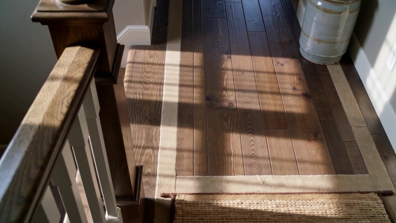 Telecamera panoramica che si muove su un pianerottolo di scale in legno a casa, mostrando un montante del corrimano, un tappeto passatoia e una fioriera.
