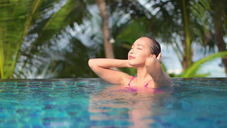 Young-woman-strokes-her-wet-hair-in-pool