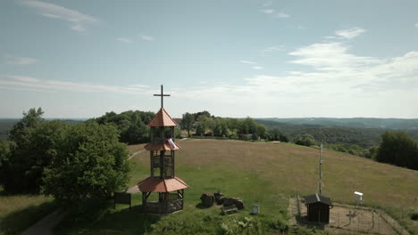 panoramic landscape shot of a hill with small tower on the top and forest with trees around them, beautiful blue sky and hills in background in slovenia, aerial drone shot