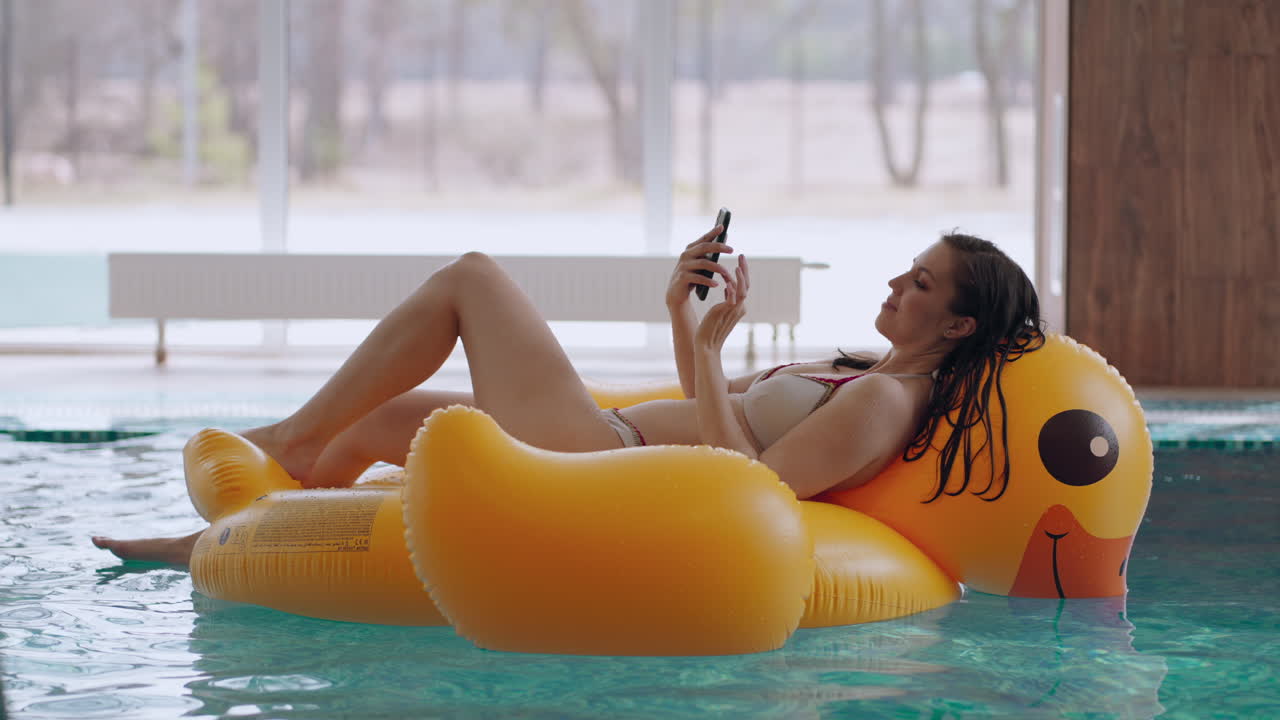 modern thermal bath center young woman in bikini is lying on inflatable swimming circle like yellow duck