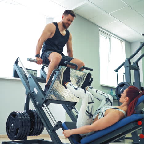 sporty girl doing exercise for legs on a modern simulator in the gym. woman is lifting man by her strong legs on a fitness machine in the light sports center.