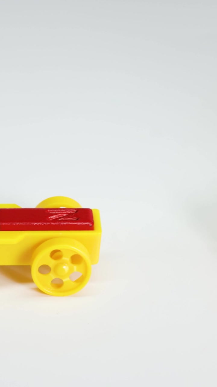 Un'automobilina giocattolo magnetica gialla rotola su uno sfondo bianco durante una dimostrazione di fisica
