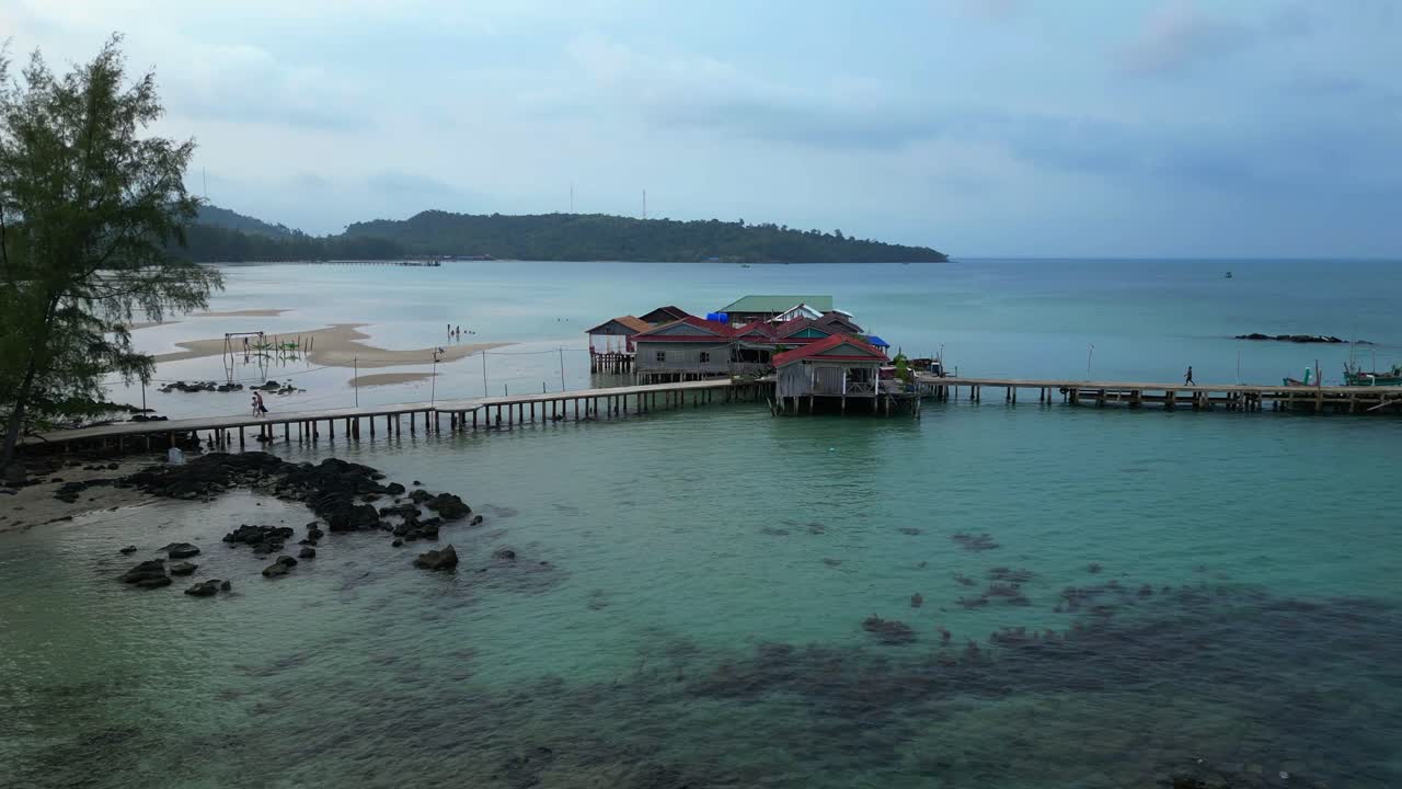 cambodia Koh Rong island, capturing the essence of tropical paradise with lush palm trees, vibrant turquoise waters, and traditional stilt houses. Fantastic aerial view static tripod hovering drone