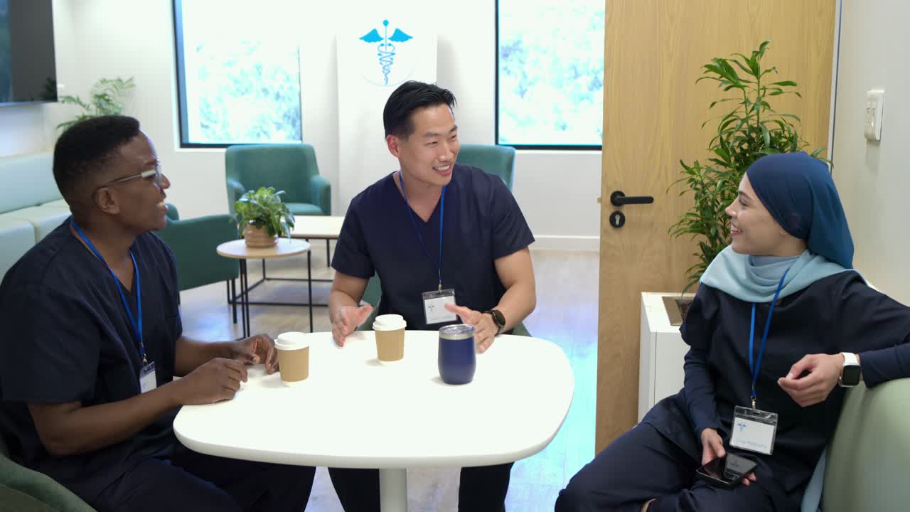 スクラブを着た多様なスタッフがおしゃべりしたり、センターで会話を始めたり、コップを持ったり、休憩中にクリニックで電話をチェックしたり。