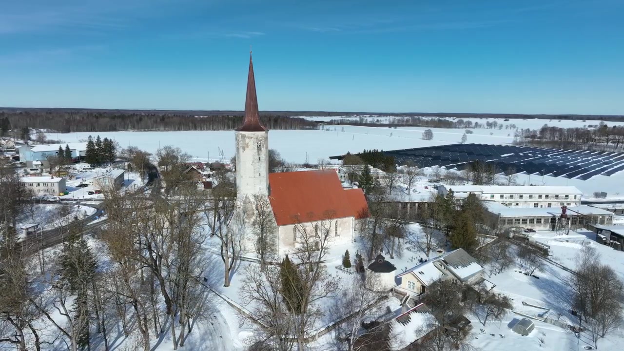 Vista aérea giratoria lentamente de la iglesia parroquial rural de San Mauricio (St. Mauritius) en Haljala, con una central de energía solar al fondo, Estonia