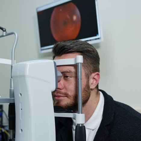 male patient visits optician. young bearded man testing his eyes in ophthalmologist office. checking the eyesight for the patient