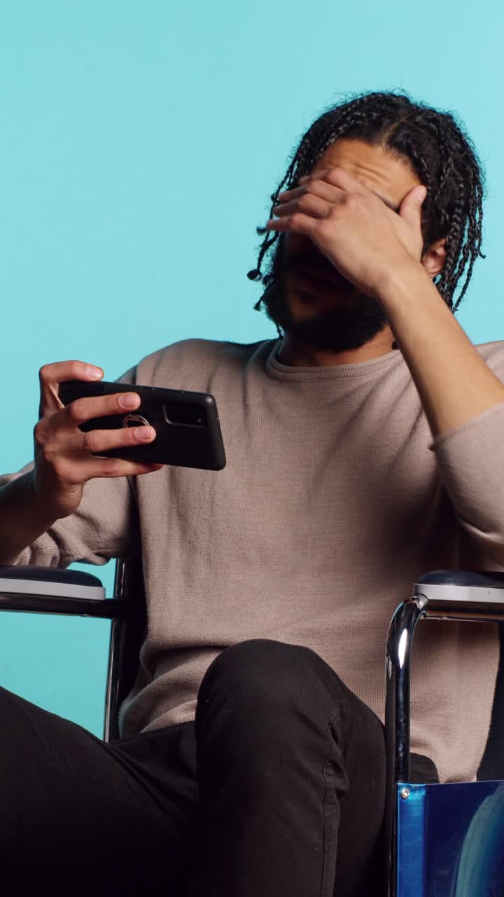 Vertical video Man in wheelchair feeling sad after losing videogame, playing on mobile phone