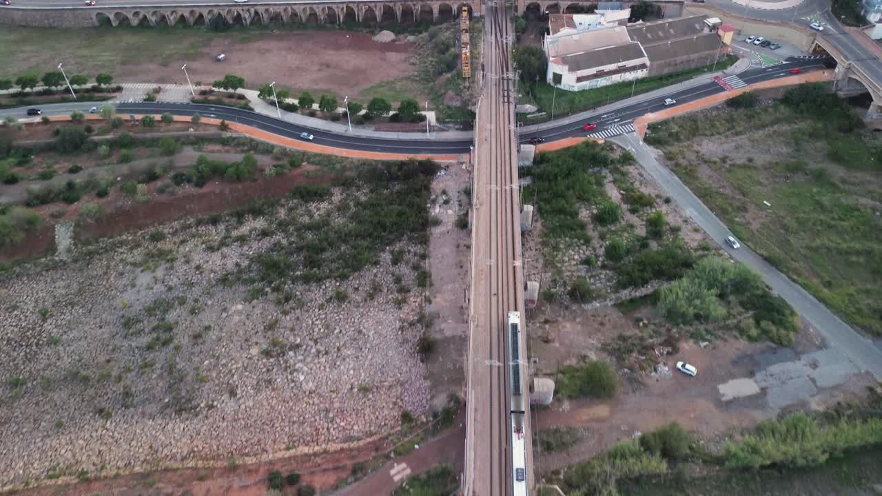 Tracking shot of a train traversing industrial areas and crossing roads with vehicles beneath at dusk