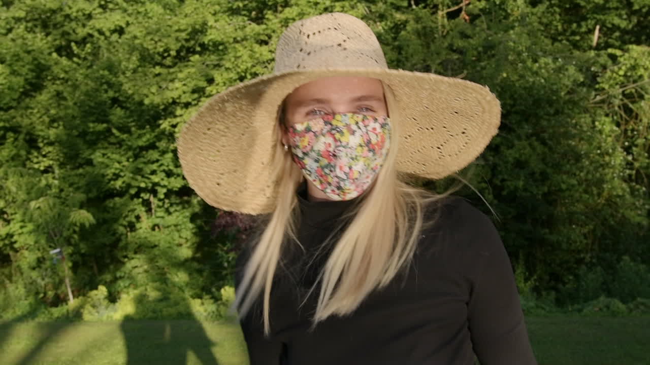 Cute woman with floral face mask making waves playfully with arms being silly on sunny day in park