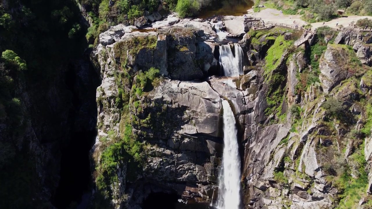Drone 4K che scende con una lenta inclinazione della telecamera verso l'alto, catturando frontalmente la maestosa doppia cascata del Pozo de los Humos a Salamanca, Spagna, in una giornata di sole splendente all'interno di un aspro canyon roccioso