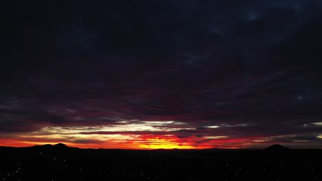 the last light of day with leaves a crimson sunset above the horizon over the mojave desert - aerial view