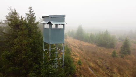 a drone pans to a watch tower in a forest filled with mist in belgium