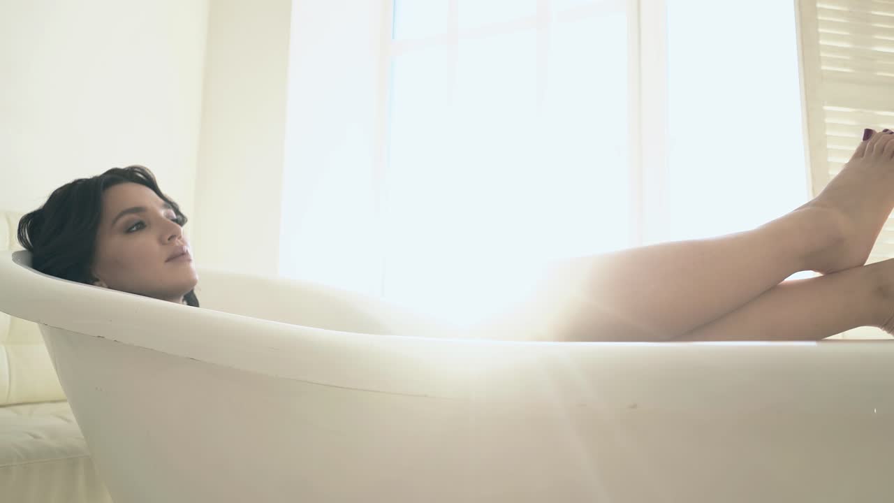 페디큐어 발을 가진 좋은 소녀는 창문에서 큰 목욕탕에서 휴식을 취합니다.