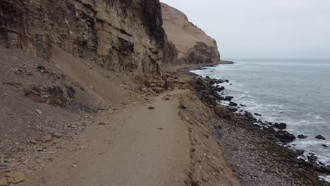 drone video of person walking down path next to cliff and rocky ocean shore