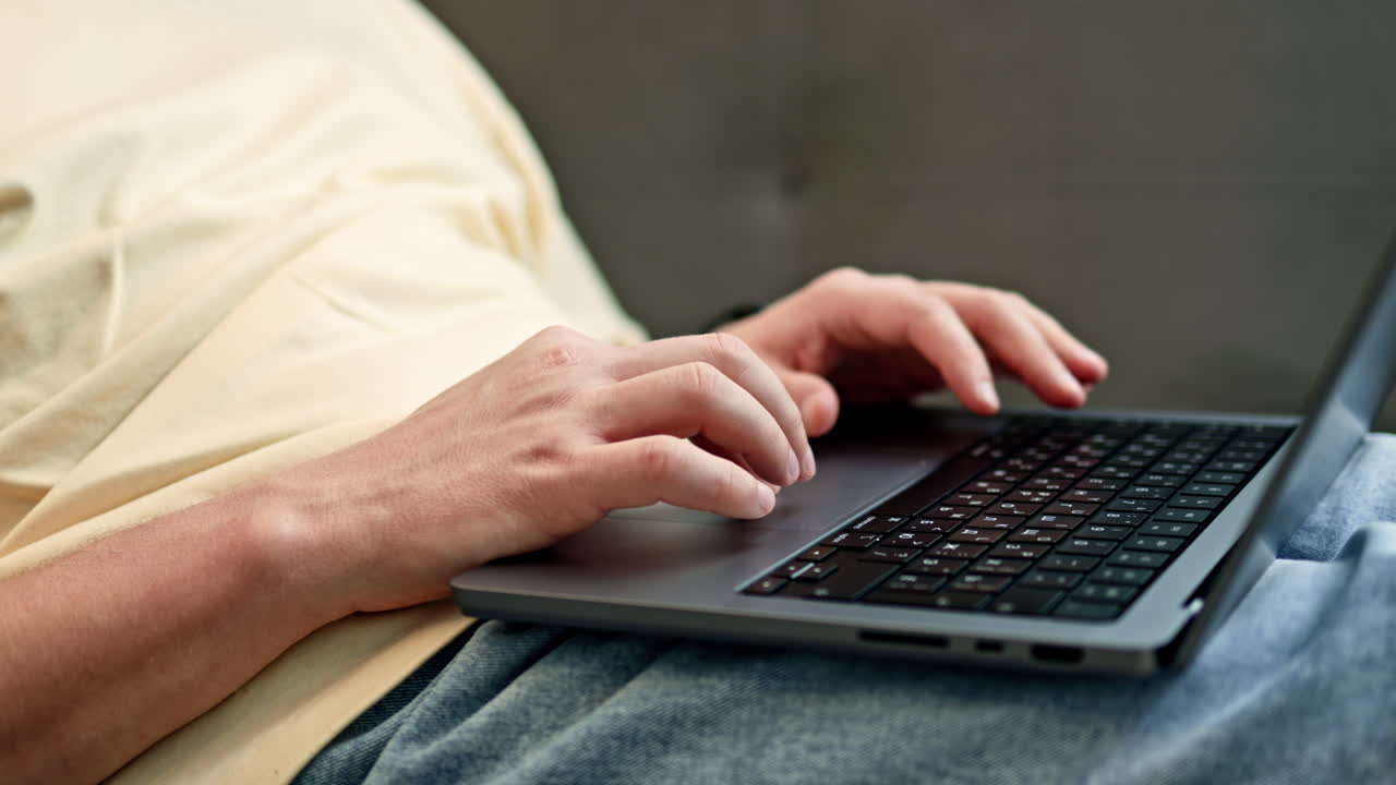 Person typing on laptop while lying down at home in the afternoon sun with a relaxed posture and casual clothing