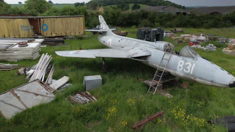 scrap hawker hunter air force fighter jet among junk in overgrown farmland pasture