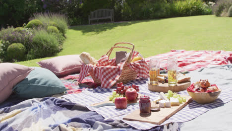 picnic hamper, food and drinks laid out on blankets in a sunny garden, slow motion