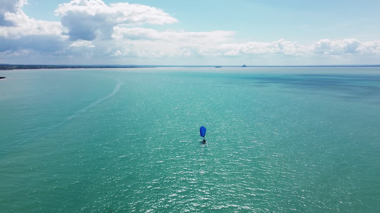 Drone footage captures a solitary sailboat gliding peacefully across the water toward Mont Saint-Michel, visible in the distant horizon