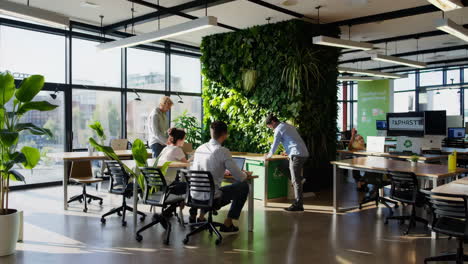 people working in a modern, sustainable office with a living green wall and recycling bins