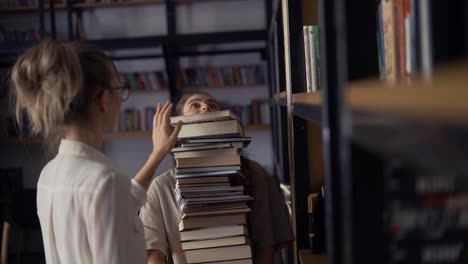 Girl-student-holding-a-lot-of-books-in-the-library,-her-friend-put-more-and-more