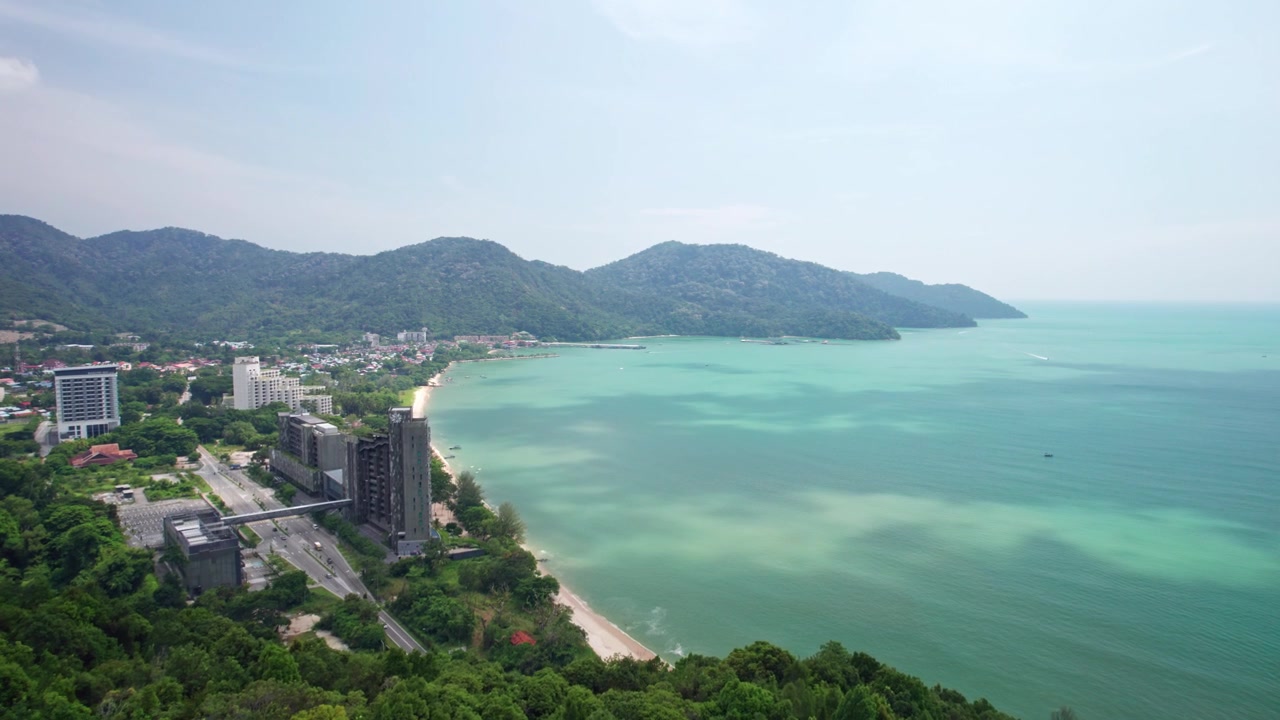 Amplias imágenes aéreas que revelan la costa tropical de Penang con desarrollo urbano, aguas turquesas y exuberante terreno montañoso que se extiende a lo largo de la costa malaya