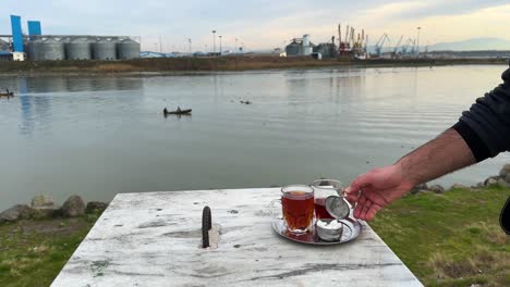 Die-Friedliche-Landschaft-Mit-Würfelzucker,-Einem-Großen-Glas-Tee-Und-Dem-Malerischen,-Unscharfen-Hintergrund-Des-Meeres-Und-Der-Fischer,-Die-Auf-Einem-Traditionellen-Holzboot-Im-Hafen-Am-Meer-In-Der-Anzali-Seelandschaft-Reiten