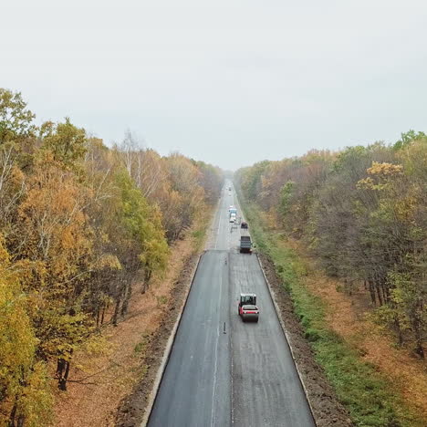 Forest road during reconstruction. Drone view along the new asphalt road with special machinery at roadworks. Camera moves forward.